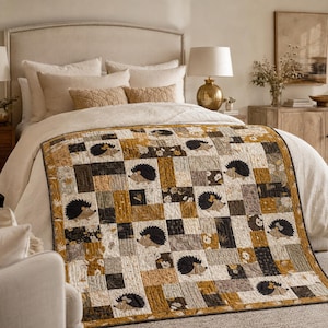 Könnte beinhalten: Eine Patchwork-Steppdecke mit einem sich wiederholenden Muster aus illustrierten Igeln in Senfgelb, Anthrazit, Creme und gedecktem Grün. Die Decke besteht aus rechteckigen Stoffblöcken mit Igelmotiven und floralen Akzenten.