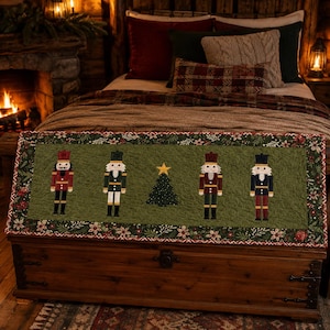 Puede incluir: Un camino de mesa de tela acolchada rectangular con un panel central de color verde oliva que presenta cuatro figuras de cascanueces y un árbol de Navidad central con una estrella amarilla. El borde muestra un patrón de flores de pascua rojas y hojas de acebo.