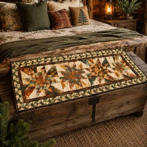 May include: A rectangular quilted table runner featuring three large star patterns in shades of forest green, burnt orange, and cream. The runner has a border of small green and cream triangles and intricate swirling stitch patterns throughout.