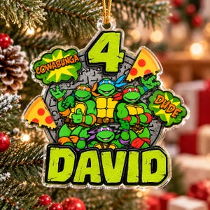 Peut inclure: Une décoration en acrylique transparent représentant les quatre Tortues Ninja, le chiffre 4 et le nom DAVID en vert lime. Le motif inclut deux parts de pizza, une bulle verte avec COWABUNGA et une autre avec DUDE.