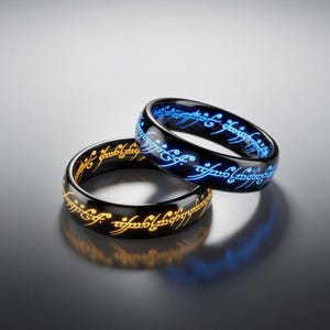 Puede incluir: Dos anillos negros con inscripciones brillantes en una escritura de fantasía. Un anillo tiene texto azul, el otro dorado. Los anillos están sobre una superficie reflectante, creando una sombra.