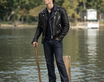 May include: A black leather motorcycle jacket with silver zippers and snaps, worn over a dark navy polo shirt and dark blue denim jeans. The outfit is paired with black leather boots and includes a wooden-handled axe held in one hand.