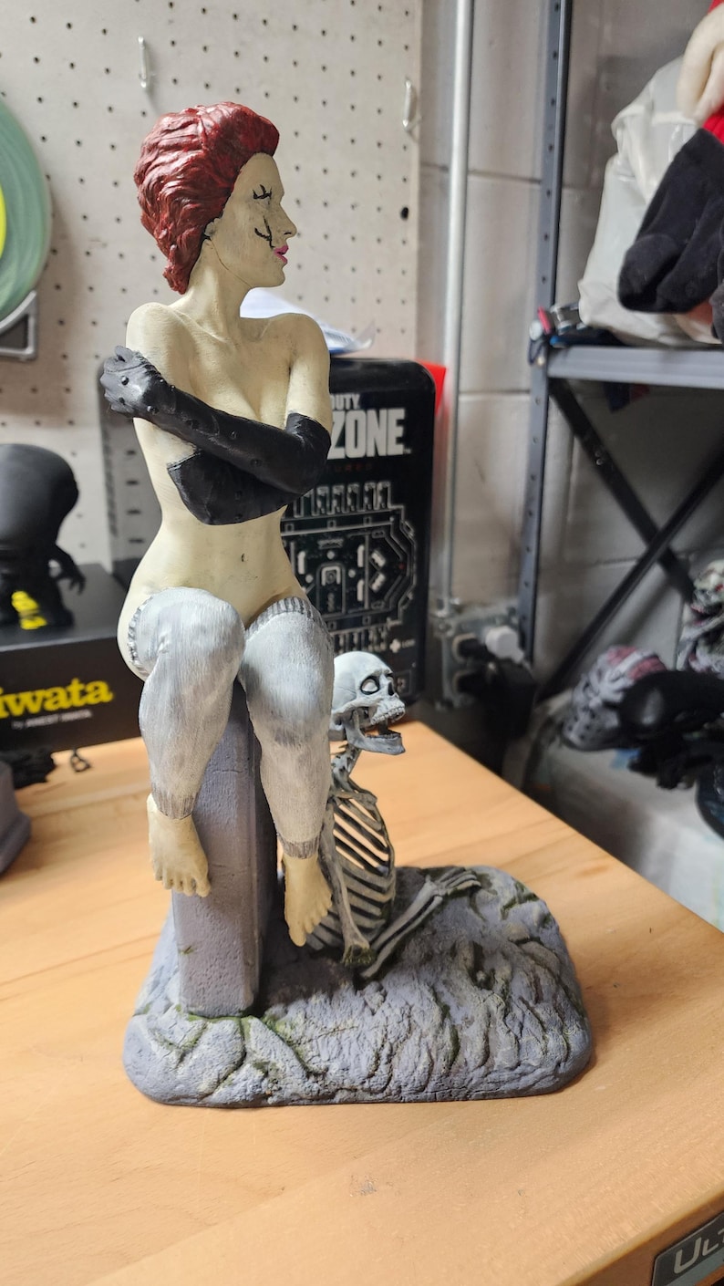 Puede incluir: Una figura pintada que muestra a un personaje con cabello corto rojo, guantes negros y medias blancas, sentado sobre un bloque gris que imita piedra. Un peque&ntilde;o esqueleto blanco se sit&uacute;a en la base del bloque sobre un suelo gris texturizado.