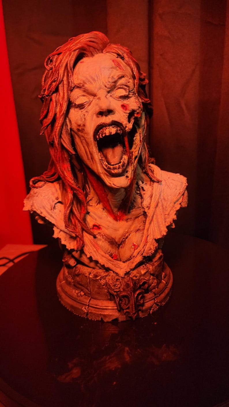 K&ouml;nnte beinhalten: Eine detaillierte B&uuml;ste einer schreienden Figur mit verfallener Haut, entbl&ouml;&szlig;ten Z&auml;hnen und langem Haar. Die Figur weist sichtbare Wunden und blutrote Akzente im Gesicht und auf der Brust auf und steht auf einem strukturierten, verwitterten Sockel.