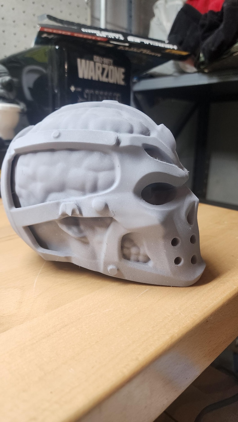 May include: A 3D printed gray resin mask featuring a skull-like structure with an exposed brain design on the sides. The mask includes a rigid frame, eye sockets, a nose cavity, and a lower section with four circular ventilation holes on the front.