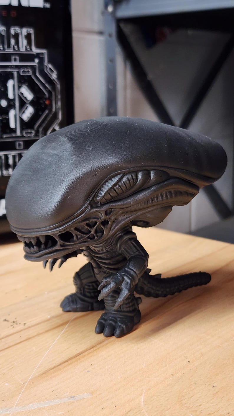 May include: A matte black figurine of a Xenomorph creature from the Alien franchise. The figure features an elongated, smooth head, a detailed skeletal torso, sharp claws, and a long tail. It stands in a crouched position with visible teeth.