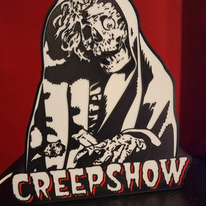 May include: A black and white 3D printed wall plaque featuring the Creepshow character with a skeletal face and hooded robe. The figure is reaching forward with a bony hand, and the word CREEPSHOW is displayed in bold white letters with red outlines.