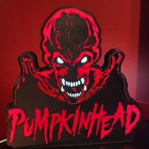 May include: A decorative LED sign featuring the Pumpkinhead character with a black and red color scheme. The creature has glowing white eyes and teeth, with the word PUMPKINHEAD written in a stylized red font at the bottom of the display.