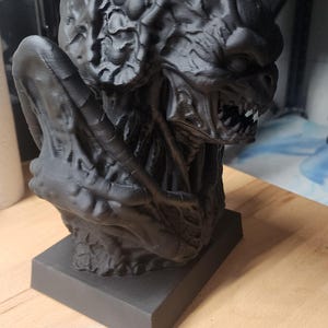 Puede incluir: Un busto negro mate impreso en 3D de una criatura con un cr&aacute;neo texturizado similar a un cerebro, dientes afilados y una mand&iacute;bula prominente. La figura presenta crestas y pliegues org&aacute;nicos complejos en toda su superficie sobre una base.