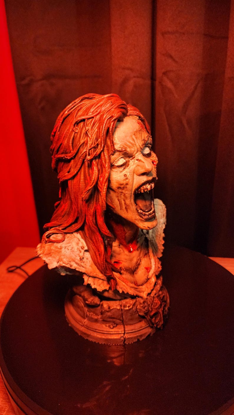 K&ouml;nnte beinhalten: Eine detaillierte B&uuml;ste einer schreienden Figur mit langem, strukturiertem rotem Haar und blasser, verwitterter Haut. Die Figur hat einen offenen Mund, der Z&auml;hne zeigt, sichtbare Gesichtsz&uuml;ge und ein zerfetztes Kleidungsst&uuml;ck auf einem Sockel.
