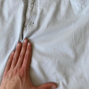 May include: Light blue pants with a button and zipper closure. The pants have pockets and belt loops. The fabric appears to be a sturdy cotton blend. The pants are slightly wrinkled.