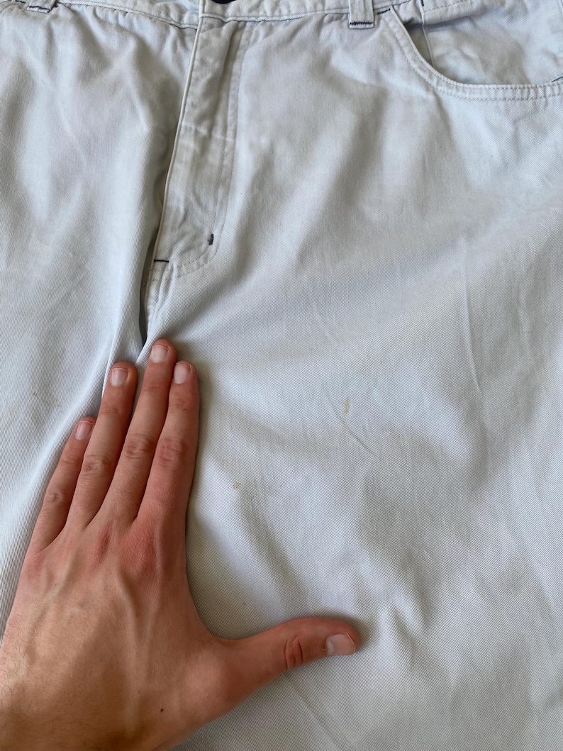 May include: Light blue pants with a button and zipper closure. The pants have pockets and belt loops. The fabric appears to be a sturdy cotton blend. The pants are slightly wrinkled.