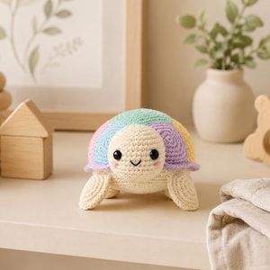 Könnte beinhalten: Ein kleines, handgefertigtes Häkel-Schildkrötenspielzeug mit cremefarbenem Kopf und Gliedmaßen sowie einem mehrfarbigen Panzer in Pastelltönen wie Rosa, Blau, Grün und Gelb. Die Schildkröte hat zwei schwarze Sicherheitsaugen und ein aufgesticktes Lächeln.