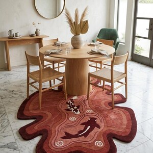 May include: An irregularly shaped area rug featuring a deep red and terracotta color palette with a wavy, organic border. The rug displays two stylized koi fish swimming amidst swirling water patterns, crafted with a textured, tufted pile surface.