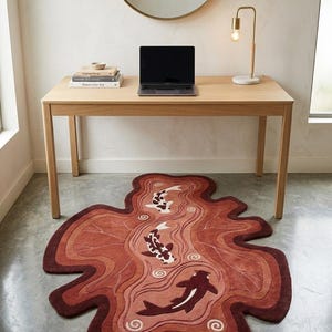 May include: An irregularly shaped area rug featuring a layered, wavy design in shades of deep red, terracotta, and rust. The rug depicts three koi fish in white, black, and dark red, swimming amidst stylized water ripples and swirling patterns.