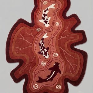 May include: An irregularly shaped rug featuring a layered, wavy design in shades of deep red and burgundy. The rug depicts three koi fish in white and dark brown, swimming amidst stylized water ripples and swirling patterns across the surface.