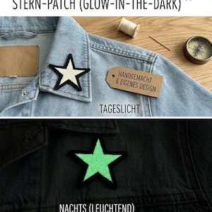 May include: A star-shaped patch with a black border attached to a light blue denim jacket. The patch appears off-white in daylight and glows a bright light green in the dark. A brown tag with the text HANDGEMACHT & EIGENES DESIGN is included.