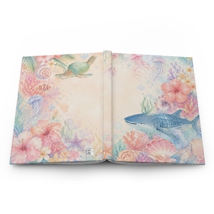 May include: Open journal with a watercolor design featuring marine life. The cover displays a sea turtle, whale shark, coral, and hibiscus flowers in shades of pink, blue, and green. The journal is open, revealing the inside pages.