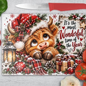 May include: A rectangular glass chopping board featuring a fluffy Highland cow wearing a Santa hat, surrounded by Christmas decorations, pinecones, and gifts. The text reads, It's the most Wonderful time of the Year, set against a rustic wood background.