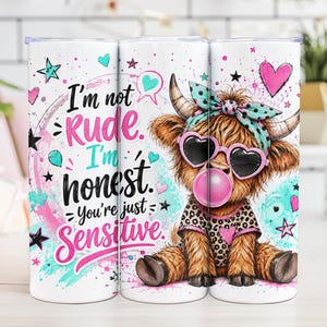 Op de afbeelding: Een witte cilindrische beker met een afbeelding van een pluizige bruine hooglander met een hartvormige zonnebril en een blauwgroene strik met stippen, die een roze kauwgombel blaast. De tekst luidt, I'm not Rude. I'm honest. You're just Sensitive.