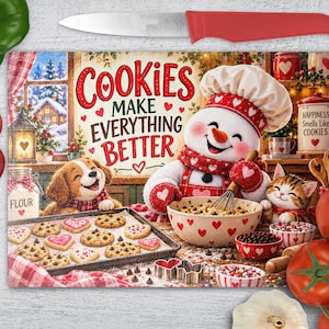 Op de afbeelding: Een rechthoekige glazen snijplank met een feestelijke illustratie van een sneeuwpop, een puppy en een kitten die koekjes bakken. De tekst luidt "COOKIES MAKE EVERYTHING BETTER" en "HAPPINESS SMELLS LIKE COOKIES". Het ontwerp bevat rode hartjes.