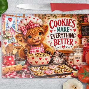 Op de afbeelding: Een rechthoekige glazen snijplank met een illustratie van een hooglandrund in een koksmuts en schort, koekjes bakkend met een kitten. De tekst luidt "COOKIES MAKE EVERYTHING BETTER" en "Happiness is Homemade". Rode hartjes versieren de afbeelding.