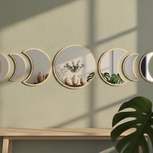 May include: A set of decorative wall mirrors in the shape of moon phases. The mirrors have a gold-colored frame and are arranged in a crescent shape. The mirrors are mounted on a light green wall, with a wooden bench below.