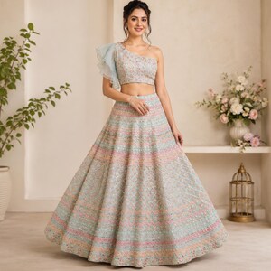 May include: A light blue two-piece ensemble featuring a cropped, one-shoulder top with a ruffled sleeve and a floor-length, flared skirt. Both pieces are heavily embellished with intricate, multi-colored embroidery and small reflective mirror accents.
