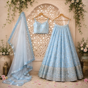 May include: A light blue three-piece ensemble consisting of a sleeveless crop top, a floor-length pleated skirt, and a sheer dupatta. The garments feature intricate silver embroidery and sequin embellishments throughout, with a wide silver border.