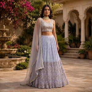 May include: A light blue pleated skirt and matching crop top with gold and floral accents. A sheer, light blue shawl with gold trim is draped over the shoulder. The outfit is worn with gold jewelry.