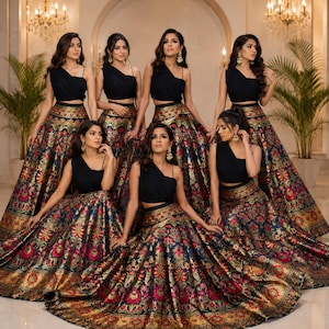 May include: A group of matching outfits consisting of a black one-shoulder crop top and a voluminous floor-length skirt featuring a dark blue base with an intricate floral pattern in shades of pink, gold, and green with a wide metallic gold border.