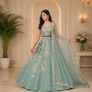 May include: A sage green floor-length lehenga choli featuring intricate silver embroidery, a sleeveless bodice, a flared skirt with vertical ruffled detailing, and a matching sheer dupatta with a decorative silver border and scattered sequins.