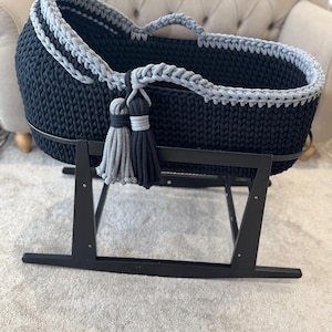 May include: A navy blue and gray crochet baby bassinet on a black rocking stand. The bassinet has a gray trim and two tassels in gray and black. The bassinet is designed for a baby.