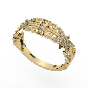 May include: A yellow gold ring featuring an intricate openwork design with swirling scroll patterns and small, round, clear stones embedded along the band and the floral-shaped focal point, creating a detailed and textured metallic appearance.