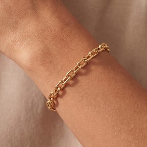 Könnte beinhalten: Ein goldfarbenes Gliederkettenarmband bestehend aus einer Reihe gleichmäßiger, länglicher ovaler Glieder, die in einer durchgehenden Schleife verbunden sind. Die Metalloberfläche hat ein poliertes, reflektierendes Finish.