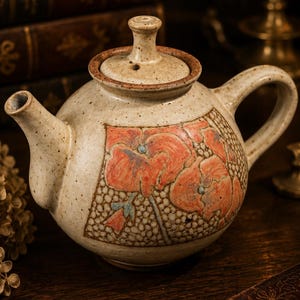 Peut inclure: Théière en céramique beige avec un couvercle et un motif floral rouge et bleu. La théière a une anse et un bec courbés. C'est un objet décoratif.