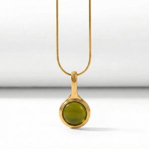 Op de afbeelding: Een goudkleurige ketting met een hanger met een ronde, olijfgroene steen. De hanger is gevat in een gouden zetting en hangt aan een fijne gouden ketting. De achtergrond is wit.