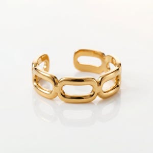 Könnte beinhalten: Ein goldfarbener Ring mit offenem Design. Der Ring hat eine Reihe von verbundenen, länglichen ovalen Formen. Der Ring besteht aus einem glänzenden, reflektierenden Metall und ist vor einem weißen Hintergrund platziert.