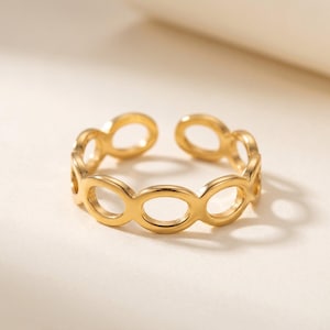 Op de afbeelding: Een goudkleurige open ring met een reeks verbonden ovale vormen. De ring is verstelbaar en ligt op een neutrale achtergrond, wat de gepolijste afwerking benadrukt. Dit sieraad is geschikt voor dagelijks gebruik.