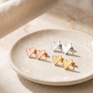Op de afbeelding: Hartvormige oorstekers in roségoud, zilver en goud. De oorbellen worden gepresenteerd op een crèmekleurige schaal, die hun eenvoudige, elegante ontwerp benadrukt. Perfect voor dagelijks gebruik of speciale gelegenheden.