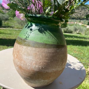 Peut inclure: Un vase en céramique bicolore, vert en haut et marron en bas, rempli de fleurs roses et de feuilles vertes. Le vase est posé sur une table ronde de couleur claire. Un objet décoratif.
