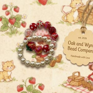 Puede incluir: Dos pulseras de cuentas con temática de fresas. Una pulsera presenta perlas de imitación blancas, mientras que la otra tiene cuentas rojas y blancas. El fondo es un patrón de fresas con una etiqueta que dice "Oak and Wyn's Bead Company".