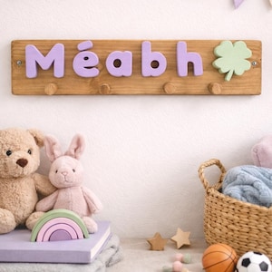 Peut inclure: Un porte-manteau mural rectangulaire en bois avec le prénom Méabh en lettres lavande en relief et une forme de trèfle vert clair. La planche en bois naturel comporte quatre petites patères rondes pour suspendre des objets.