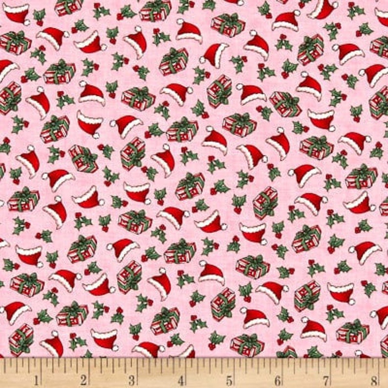 Puede incluir: Tela rosa con un patr&oacute;n repetido de regalos de Navidad rojos y blancos y gorros de Pap&aacute; Noel. El patr&oacute;n est&aacute; sobre un fondo rosa con hojas de acebo verdes.