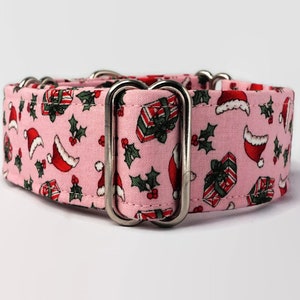 Puede incluir: Collar de perro rosa con estampado navide&ntilde;o con gorros de Pap&aacute; Noel, acebo y regalos. El collar tiene herrajes met&aacute;licos plateados.