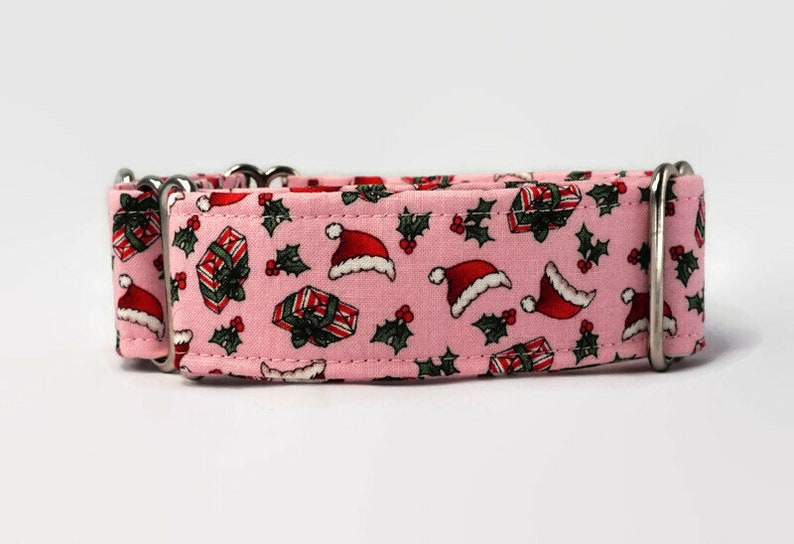 Puede incluir: Collar de perro rosa con un patr&oacute;n navide&ntilde;o con gorros de Pap&aacute; Noel, regalos y acebo.