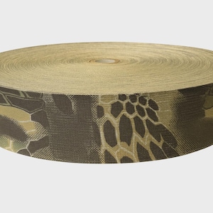 May include: A roll of heavy-duty nylon webbing featuring a brown, tan, and dark green camouflage pattern with a distinct hexagonal grid design. The material has a tightly woven, textured surface and is coiled into a flat, circular spool shape.