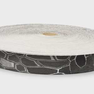 May include: A circular roll of flat webbing tape featuring a black and dark gray hexagonal camouflage pattern. The top surface of the roll is white, while the outer edge displays the repeating geometric print with thin white lines.