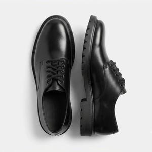Peut inclure: Une paire de chaussures derby en cuir noir avec une finition lisse, des bouts arrondis et des lacets noirs. Les chaussures présentent une semelle épaisse en caoutchouc cranté avec un motif profond, offrant une base solide à la silhouette basse.