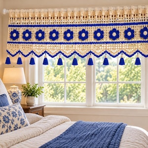 Puede incluir: Una cenefa de ganchillo color crema para ventana que presenta una fila horizontal de motivos florales azul vibrante, patrones calados intrincados y un borde inferior festoneado con doce borlas azules a juego colgando del adorno.